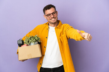 Young caucasian man making a move while picking up a box full of things isolated on purple...