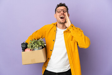 Young caucasian man making a move while picking up a box full of things isolated on purple...