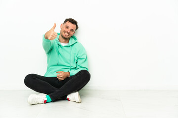 Fototapeta premium Young handsome caucasian man sitting on the floor with thumbs up because something good has happened