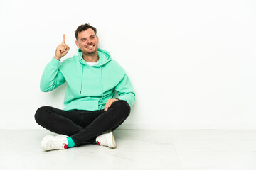 Fototapeta premium Young handsome caucasian man sitting on the floor intending to realizes the solution while lifting a finger up
