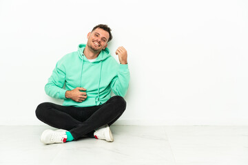Young handsome caucasian man sitting on the floor making guitar gesture