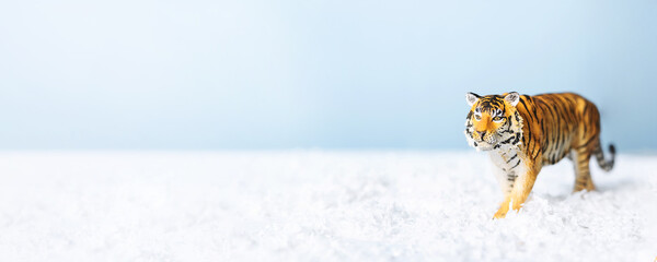 Tiger symbol of the Chinese new year 2022. Figurine of tiger in snow on blue background. Christmas greeting card. Banner, copy space.