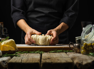 The chef kneads the dough on a cutting board. Ingredients for the preparation of dough products - spaghetti, pasta. pizza, pie, focaccia. Black background, country style. Home cooking, hotel..