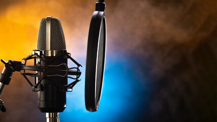 Professional studio microphone and pop filter on a beautiful yellow-blue smoky background. Night club, concert, radio broadcasting, television, recording studio, purity of sound, vocals, music.