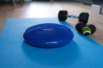 Blue balance cushion lying on mat near dumbbells and roll ball home closeup