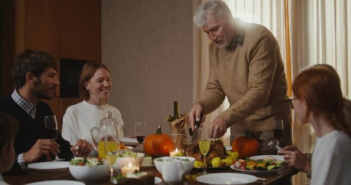 father of family cuts turkey and distributes piece to everyone in Thanksgiving