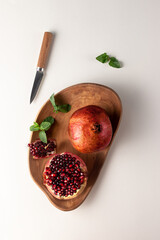 food composition with cut red pomegranate on a wooden plate top view. fresh mint and knife isolated...