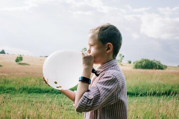 smartly dressed boy blowing up a balloon at a wedding in summer