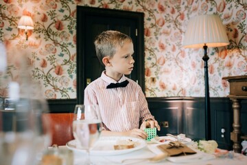 boy dressed in a shirt and bow tie playing at a wedding