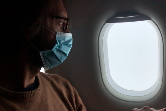 Man wears a face mask and look the sky by an airplane window, pandemic