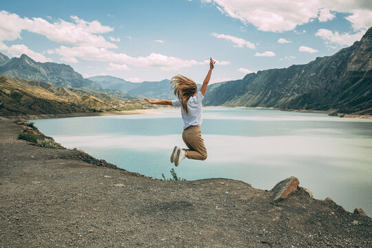 The girl full of joy jumps against the background of mountains