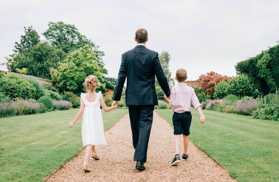 father and kids dressed for a wedding walking in a beautiful garden