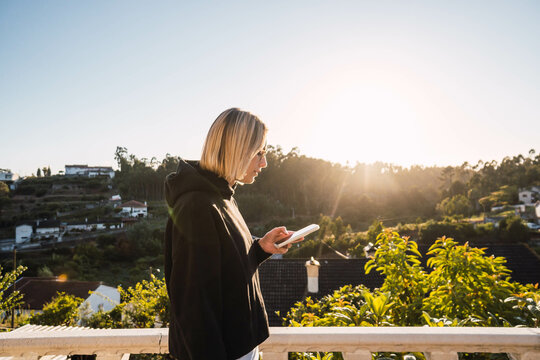 blonde woman looking at the mobile on a gazebo against sunset