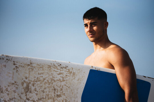 Young man holding his surfboard on the beach.