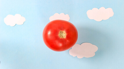 A red ripe tomato flies across a paper sky with paper clouds.