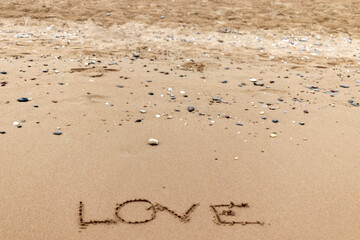 'love' lettering on the beach is drawn on the yellow sands on the shore. Valentine's Day.