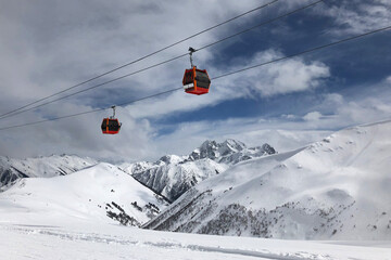 Two red gondolas on sky and cloudly background lift people in high mountains. Active winter leasure concept. - obrazy, fototapety, plakaty