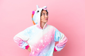 Young caucasian woman with unicorn pajamas isolated on pink background and looking up