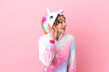 Young caucasian woman with unicorn pajamas isolated on pink background listening to something by putting hand on the ear © luismolinero