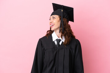 Young university graduate woman isolated on pink background looking side