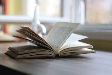 Candle in a skull shaped candle holder and open book on a table. Dark academia concept. Selective focus.