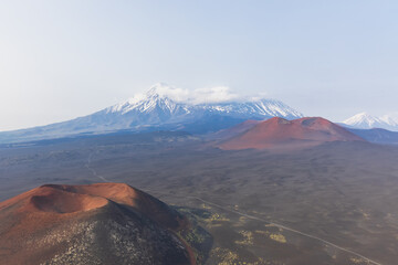 Kamchatka rocks from volcanic rocks multi-colored volcanic rocks. Crumbling volcano craters. against the backdrop of volcanoes with peaks in the snow and clouds. Ostry Tolbachik and Plosky Tolbachik. - obrazy, fototapety, plakaty