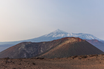 Kamchatka rocks from volcanic rocks multi-colored volcanic rocks. Crumbling volcano craters. against the backdrop of volcanoes with peaks in the snow and clouds. Ostry Tolbachik and Plosky Tolbachik. - obrazy, fototapety, plakaty