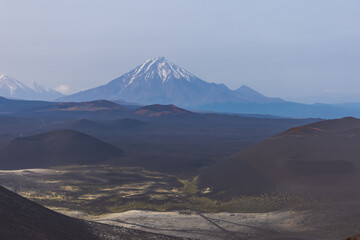 Kamchatka rocks from volcanic rocks multi-colored volcanic rocks. Crumbling volcano craters. against the backdrop of volcanoes with peaks in the snow and clouds. Ostry Tolbachik and Plosky Tolbachik. - obrazy, fototapety, plakaty