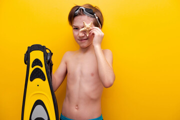 Close-up boy with flippers and starfish with yellow background. Traveling on vacation at sea with children. Summer vacation at school basis for banner - obrazy, fototapety, plakaty