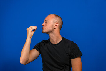 Happy business man licking fingers isolated on blue studio background. Beautiful male half-length portrait. Young satisfy man. Human emotions, facial expression concept. Front view.