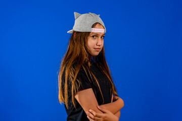 Picture of angry little girl child standing isolated over blue background. Looking camera with arms crossed