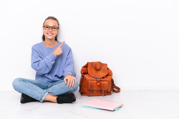 Young student girl sitting one the floor isolated on white background pointing to the side to...
