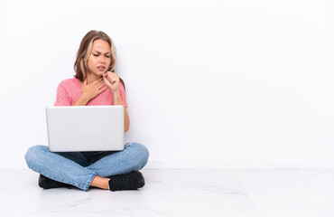 Young Russian girl with a laptop sitting on the floor isolated on white background is suffering...