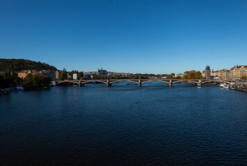 La Vltava, Moldau, se dirige vers le château de Prague. Un pont est au premier plan. Il fait beau, le ciel est bleu sans nuages.