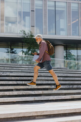 Obraz premium an adult gray-haired man with a beard goes to the office to work. a senior businessman in a shirt and with a laptop is making a career in a large company. a stylish European talks on the phone with