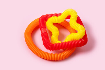Colorful anti-stress fidget push pop tube sensory toys for children on pink background. Top view, flat lay. Close-up of creative game with popular plastic flexible bright corrugated pipe.