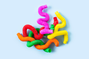 Colorful anti-stress fidget push pop tube sensory toys for children on blue background. Top view, flat lay. Close-up of creative game with popular plastic flexible bright corrugated pipe.