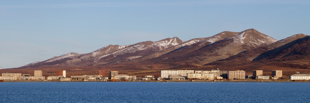 Panorama of an abandoned port town. View from the sea to the coast, abandoned buildings and mountains. An old coastal village. Beringovsky settlement, Bering Sea, Chukotka, Siberia, Far East Russia.