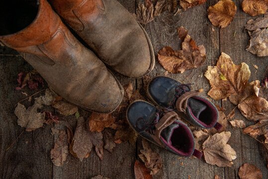 Old work boots and child boots on wooden floor with Fall leaves