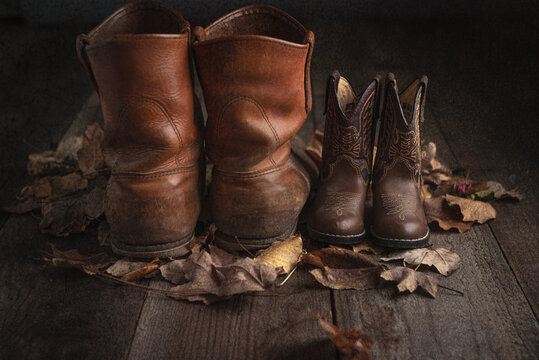 work boots and child cowboy boots on wooden floor with fall leaves