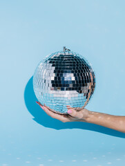Shiny disco ball in a woman's hand isolated on a bright blue background. Ball part effect,...