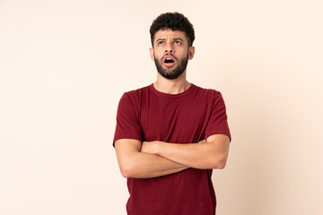 Young Moroccan man isolated on beige background looking up and with surprised expression