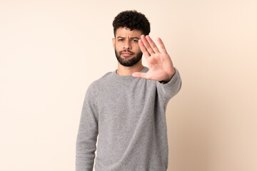 Young Moroccan man isolated on beige background making stop gesture