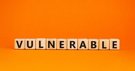 Vulnerable symbol. The word Vulnerable on wooden cubes. Beautiful orange table, orange background. Business and vulnerable concept. Copy space.