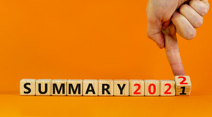 Symbol of planning 2022 summary new year. Businessman turns a wooden cube and changes words 'summary 2021' to 'summary 2022'. Beautiful orange background, copy space. Business, 2022 summary concept.