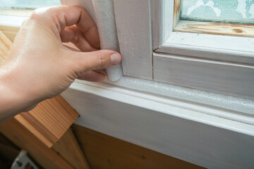 Woman hand insulating old windows to prevent warmth heat leak and drafts, preparing house for...