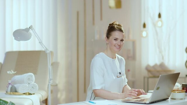 smiling 40 years old woman employee with laptop in modern beauty studio.