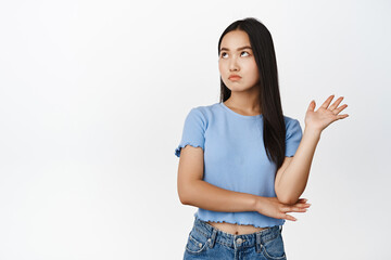 Annoyed arrogant asian woman roll eyes, looking away and wave hand to decline smth bothering her,...
