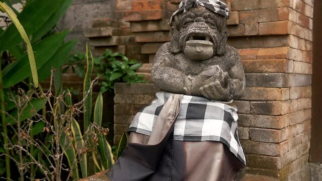 Alex Ancient stone sculpture near brick wall. Statue of unhuman look with roots to local mythology, adorned with headscarf and a skirt by the locals. Sculpture helping tourists to feel regional