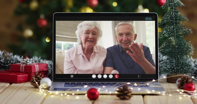 Caucasian senior couple waving on video call on laptop, with christmas tree
